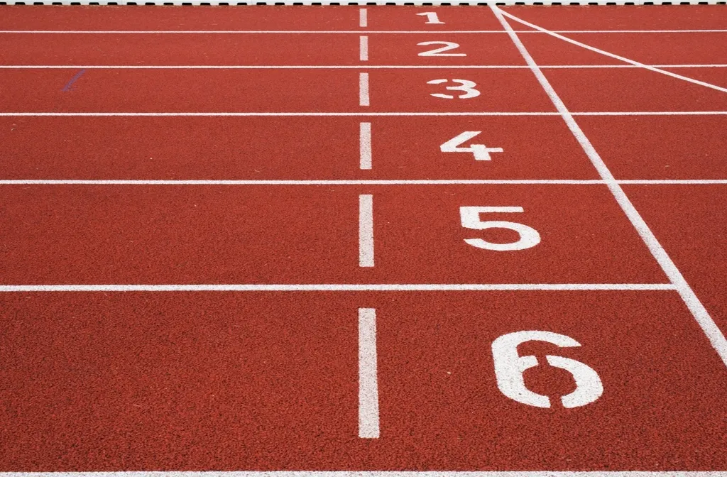 Calles numeradas del uno al seis pintadas en blanco sobre el pavimento sintético rojo de una pista de atletismo