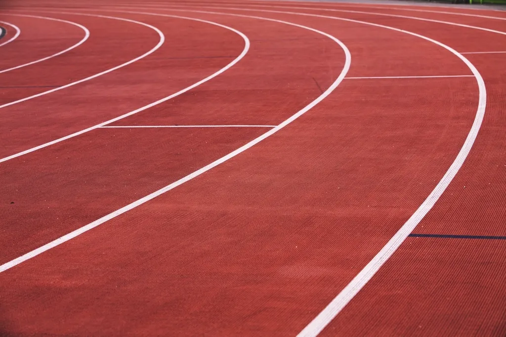 Detalle de la curva de una pista de atletismo con las líneas blancas de separación de calles sobre el pavimento rojo
