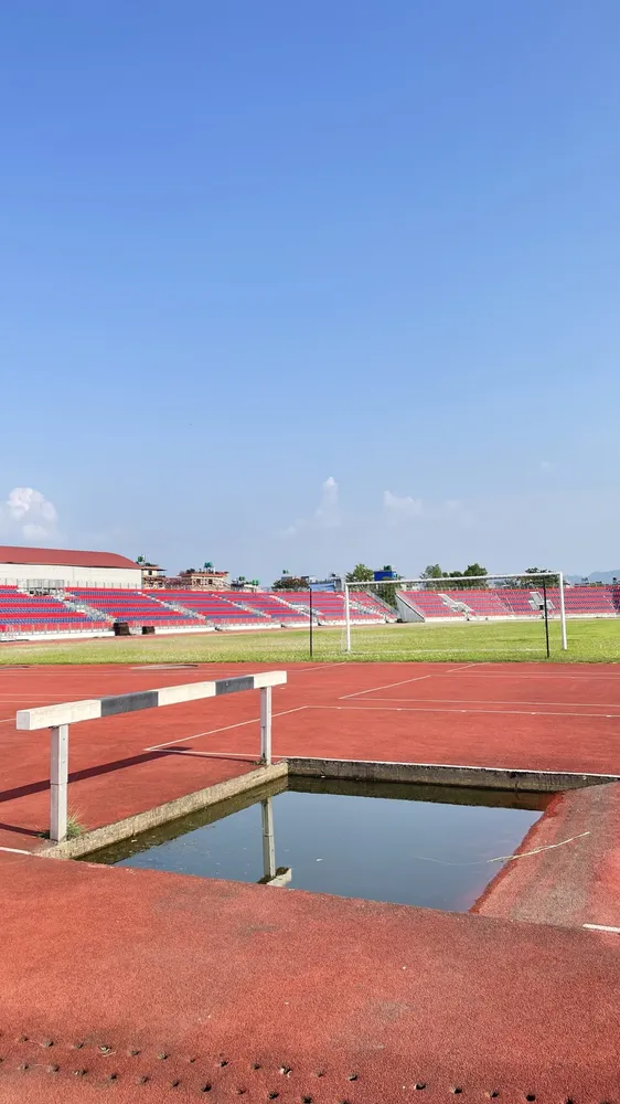 Ría de obstáculos con su valla fija en una pista de atletismo vacía, con las gradas al fondo bajo un cielo despejado