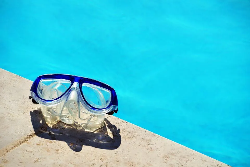 Unas gafas de natación apoyadas sobre el bordillo de hormigón junto al agua azul de una piscina