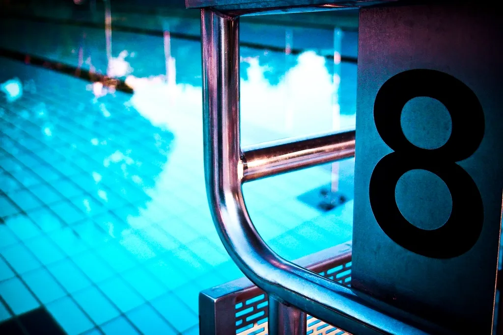 Poyete de salida numerado con un ocho junto al agua iluminada de una piscina cubierta