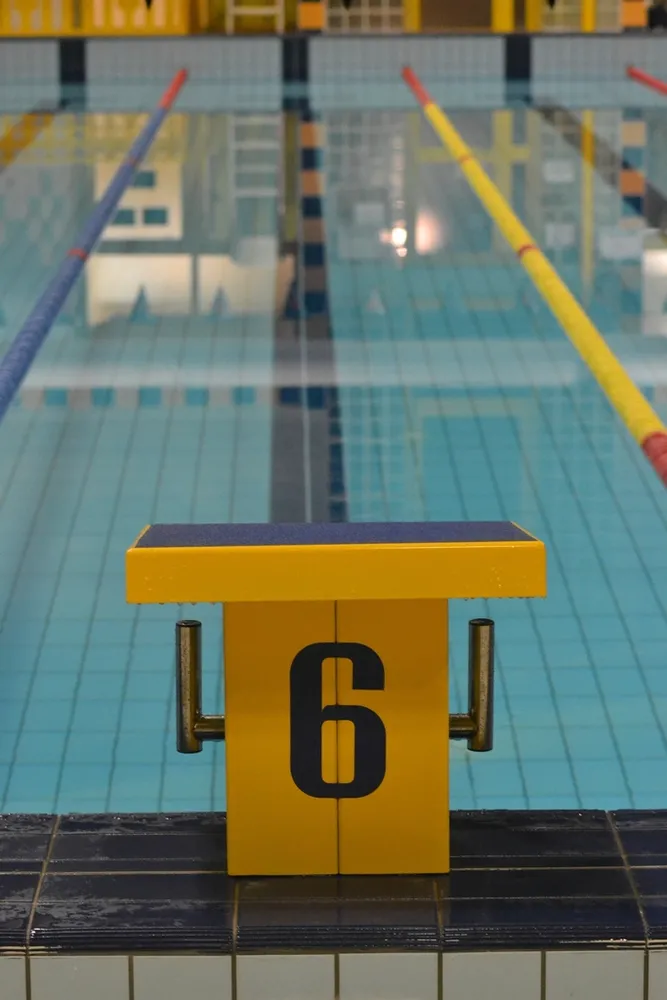 Poyete de salida amarillo con el número seis situado en el bordillo de una piscina cubierta con las corcheras colocadas