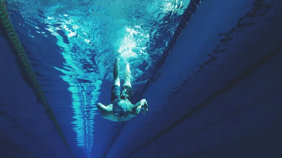 Vista submarina de una calle de piscina con una persona nadando en posición horizontal tras impulsarse de la pared